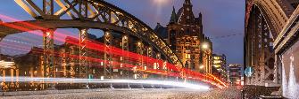 
Dynamické svetelné stopy áut za súmraku na moste v skladovej štvrti Speicherstadt v Hamburgu