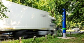 
Egy tehergépkocsi főútvonalon halad el a Toll Collect kék színű ellenőrző oszlopa mellett.