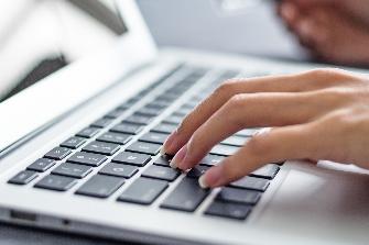 
Hände tippen Daten für die Online-Einbuchung in einen Laptop