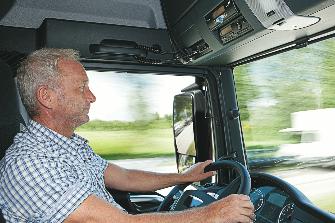 
A truck driver sits at the steering wheel; an OBU is installed above the windscreen
