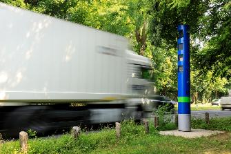 
Egy tehergépkocsi főútvonalon halad el a Toll Collect kék színű ellenőrző oszlopa mellett.
