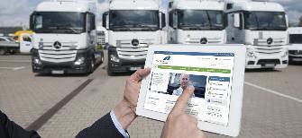 
Un transportista sujeta una tablet delante de su camión; la pantalla muestra el portal del cliente de Toll Collect.