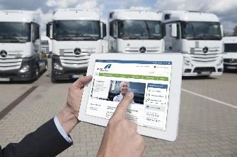 
Spedytor stojący przed samochodem ciężarowym trzyma tablet, na którego ekranie wyświetlony jest portal klienta Toll Collect.