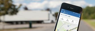 
Op het scherm van een smartphone wordt de Toll Collect-app weergegeven. Op de achtergrond parkeert een vrachtwagen.